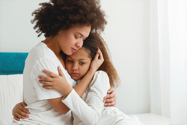 Mother Comforting Her Daughter Sitting In The Bedroom Hugging 